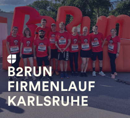 Gruppe von Mitarbeitenden in roten Laufshirts beim B2Run Firmenlauf Karlsruhe, gemeinsam vor dem Start-/Zielbogen stehend.