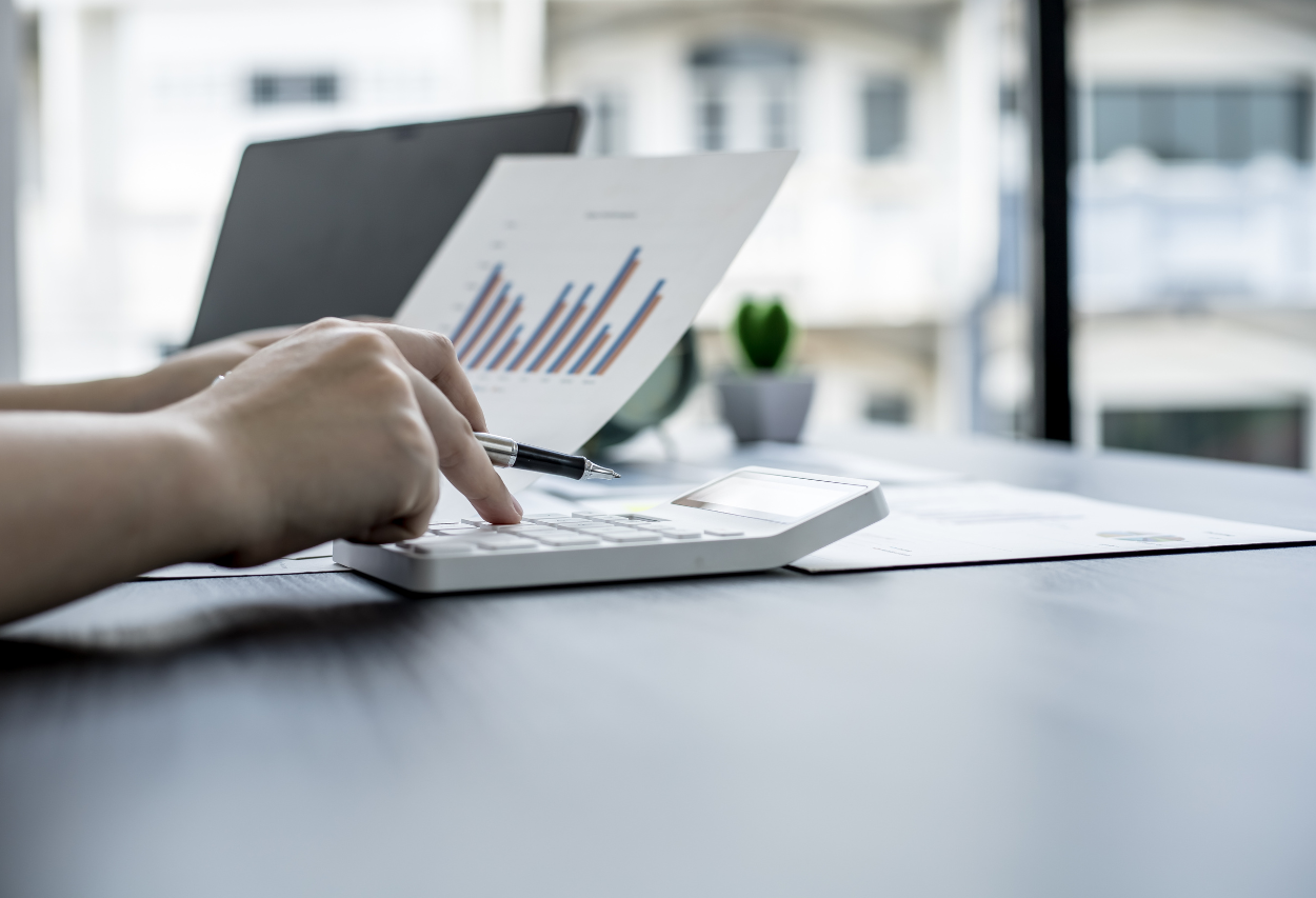 Eine Person berechnet Kennzahlen mit Taschenrechner und analysiert Diagramme am Arbeitsplatz, symbolisch für finanzielle Analyse