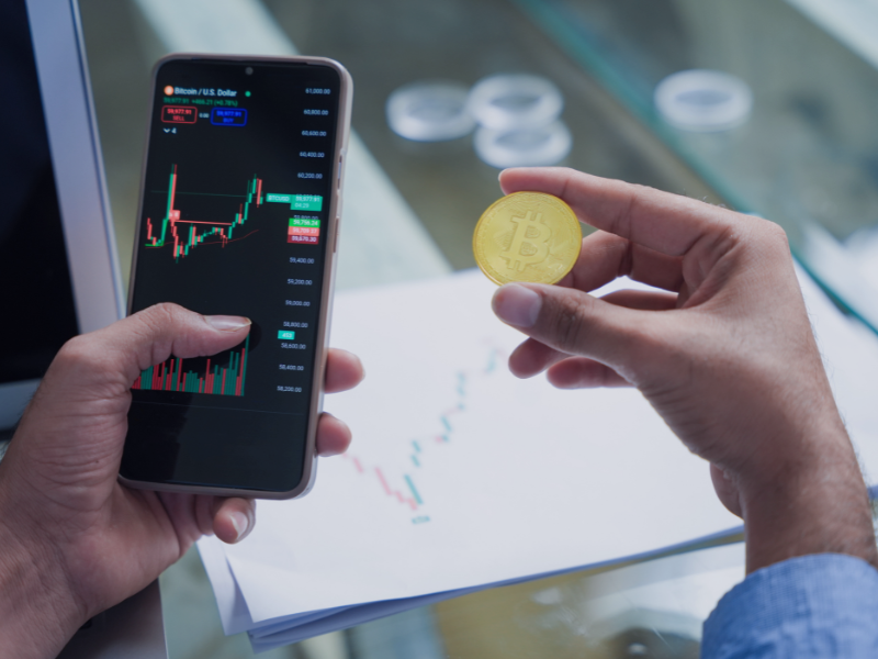 Smartphone mit Kurschart und Bitcoin in der Hand, symbolisch für okenisierung als Innovationstreiber im Kapitalmarkt