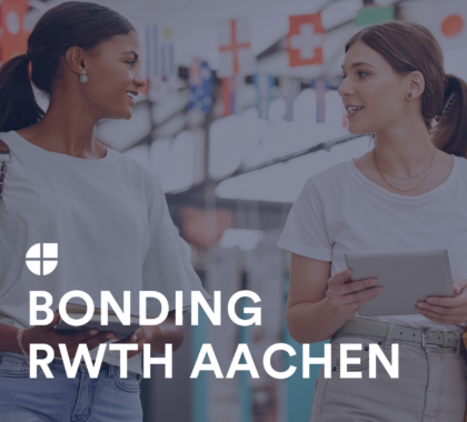 Zwei junge Frauen unterhalten sich lächelnd in einer modernen Umgebung mit internationalen Flaggen im Hintergrund, symbolisch für „Bonding RWTH Aachen“.