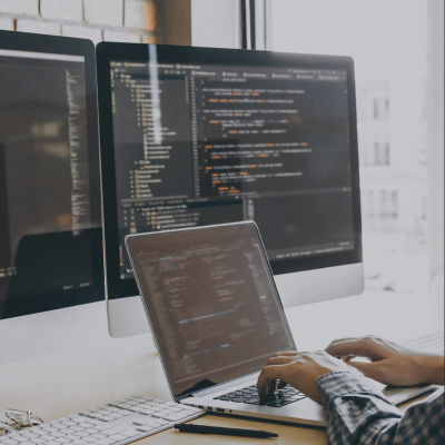 Person arbeitet an Laptop und externem Monitor mit Code, symbolisch für Consileon Softwareentwicklung