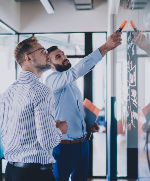 Zwei Kollegen stehen vor Whiteboard und diskutieren, symbolisch für IT-Projektmanagement