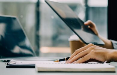 Person arbeitet im Büro am Laptop und Ipad, symbolisch für Vergütungssysteme