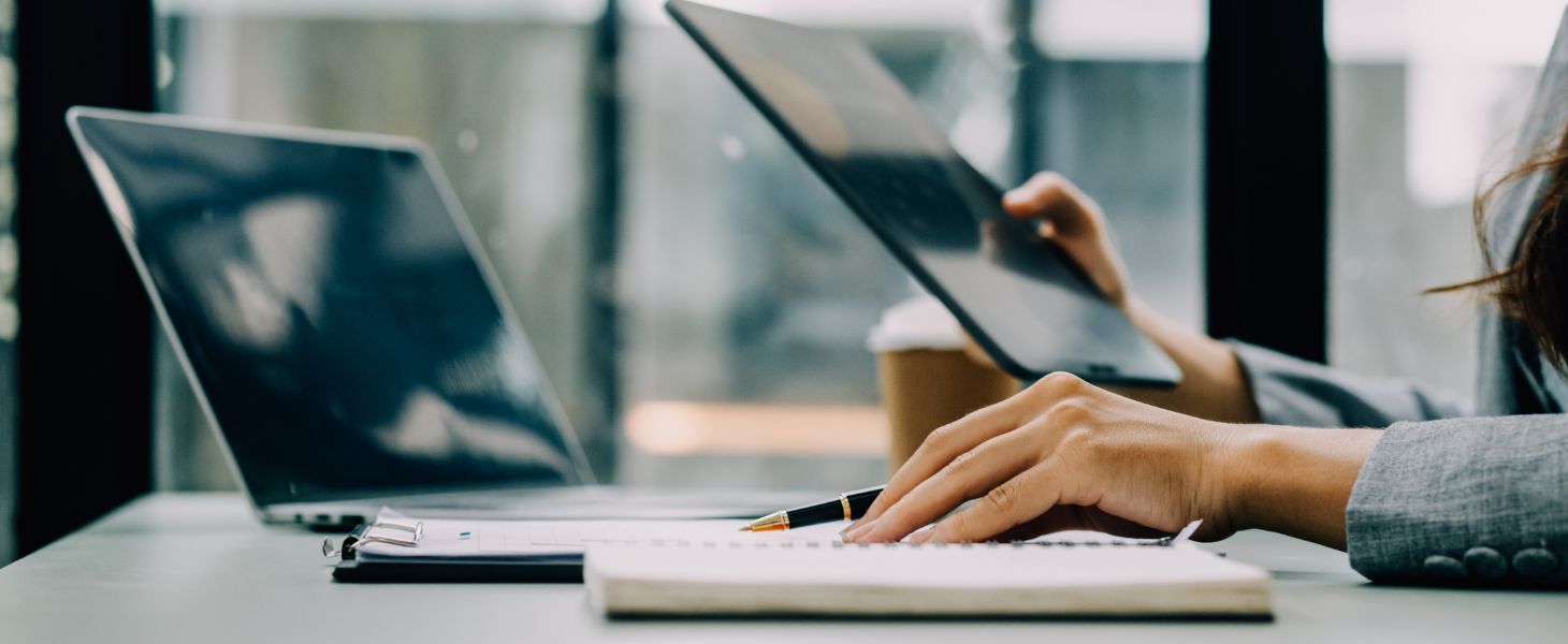 Person arbeitet im Büro am Laptop und Ipad, symbolisch für Vergütungssysteme