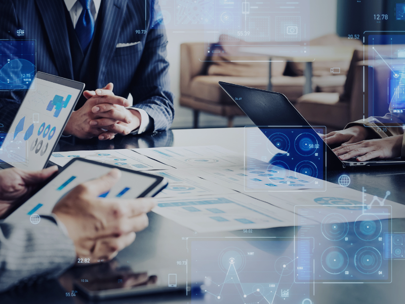 Geschäftsleute besprechen an einem Tisch Diagramme und digitale Auswertungen auf Tablet und Laptop, symbolisch für Consileon IT-Beratung für Digital Due Diligence